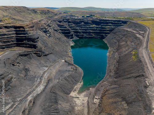 Aerial view over massive disused surface coal mine, steep terraced walls surrounding deep flooded pit, former industrial extraction site undergoing natural filling