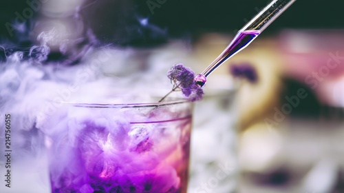 Close up of a glass with a purple liquid and a dropper generating smoke