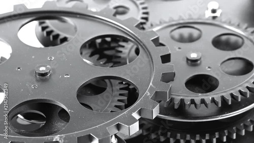 Macro close-up shot of dark metallic cogs and gearwheels meshing together within a complex mechanical assembly, symbolizing precision engineering, industrial efficiency, teamwork, and automated machin