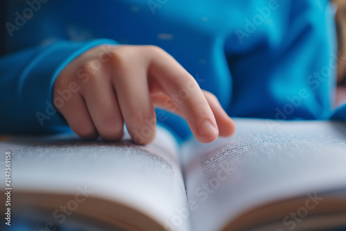 Close up of a child's hand pointing at words while reading an open book