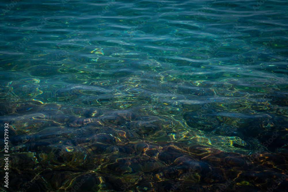 Fototapeta premium Crystal clear water surface texture with sun caustic reflections on the rocky sea floor