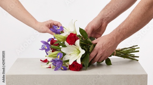 Two hands arranging a beautiful bouquet of colorful flowers, symbolizing love and care. The arrangement includes white lilies, red roses, and purple irises, creating a vibrant display