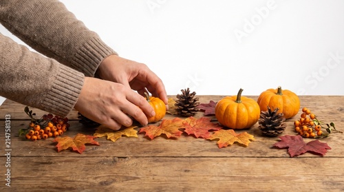 Hands arranging autumn decoration with mini pumpkin, pinecone and colorful fall leaves on a wooden table. Fall season and harvest festival vibes.