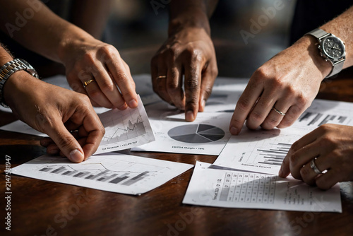 Close-up of diverse hands analyzing financial charts and graphs on a wooden table, concept for business meeting, data analysis and strategic planning