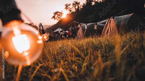 At dusk, the camping tents on the green grass are illuminated by local industrial outdoor lights, with a close-up shot of the warm light.