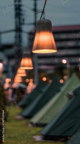 At dusk, the camping tents on the green grass are illuminated by local industrial outdoor lights, with a close-up shot of the warm light.