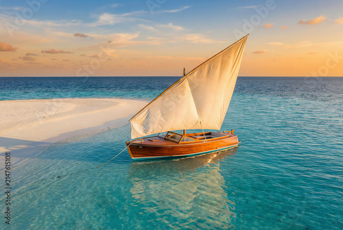 Traditional wooden sailboat on clear tropical water near sandbar