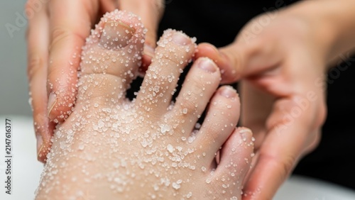 Hands gently exfoliating a foot covered in granular substance. Closeup, spa treatment