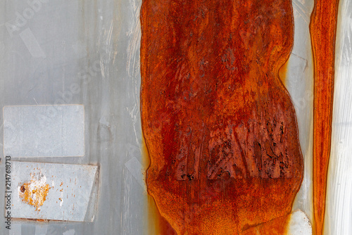 Heavily corroded metal sheet with dark orange rust and old sticker residue