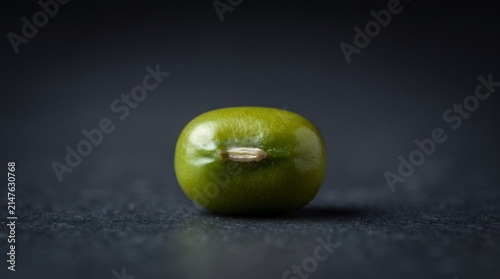 A vibrant green mung bean, seen from a slightly elevated perspective, isolated on a dark, understated surface.