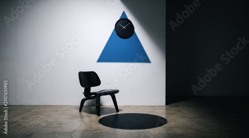 A minimalist room features a black chair casting a circular shadow against a white wall with a blue triangular accent and a clock.