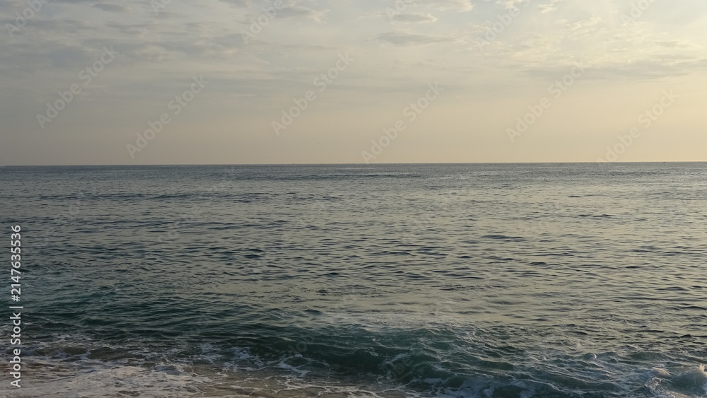 Fototapeta premium Serene Ocean View Under Soft Early Morning Sky. A calm blue sea with subtle wave motion under a soft morning sky shortly along the East Coast of Gangneung, South Korea.