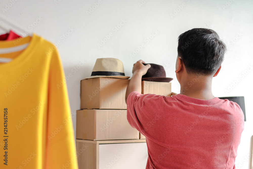 Obraz premium Rear View of Asian Man Arranging Hats and Package Boxes on Shelf for Online Store Business