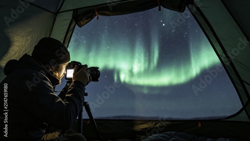 Photography enthusiast in tent capturing aurora through mesh