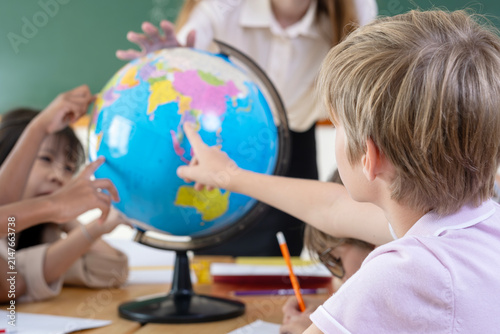 Obraz na plátně Smiling female teacher guiding elementary students with a world globe