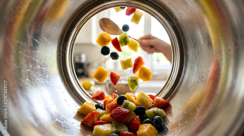 Fruit Pieces Being Added to a Blender Jar with Fresh Strawberries, Kiwi, Pineapple, and Blackberries for Smoothie Preparation in a Modern Kitchen