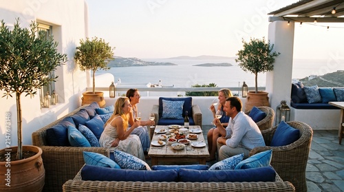 Mediterranean terrace lounge area, whitewashed walls, blue accent cushions, wicker furniture, potted olive trees, ocean view backdrop