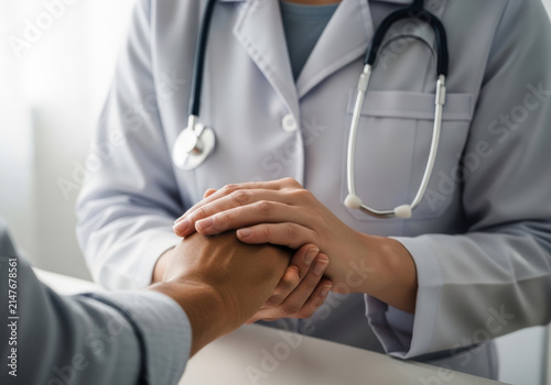 Professional doctor offering support to patient by holding hands gently as sign of compassion empathy comfort and medical care in hospital.