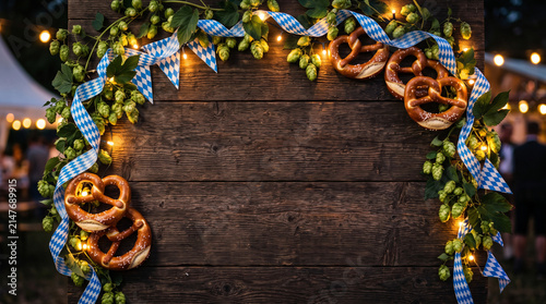Oktoberfest wooden board background decorated with pretzels, fresh hops, blue ribbon and fairy lights
