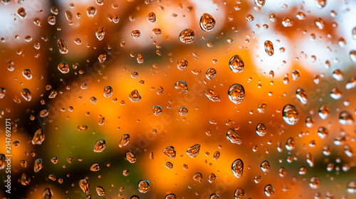 Raindrops clinging to a glass surface with blurred orange autumn foliage