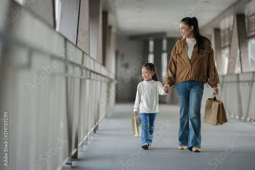 happy mother and child girl with shopping bag walking on footbridge in city