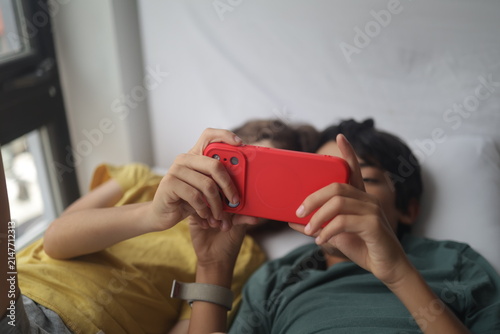 Two boys sharing a smartphone in a red case. Looking at the screen together