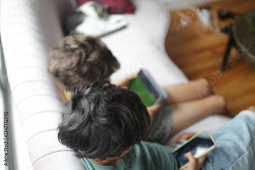 Obraz na plátně Children absorbed in screen time, sitting on a sofa while interacting with their