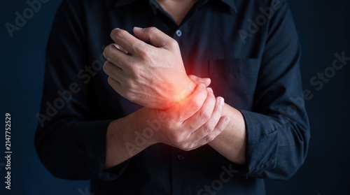 Man holding painful wrist with red glowing effect indicating injury or arthritis pain against dark blue background representing health issues and medical concept