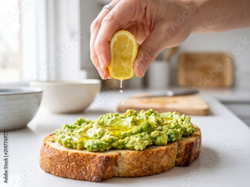 Close up of hand squeezing fresh lemon juice over avocado toast on kitchen counter