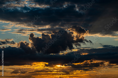 Golden sunset behind dramatic dark clouds. Dramatic sunset sky with bright orange light breaking through heavy dark storm clouds. Nature background