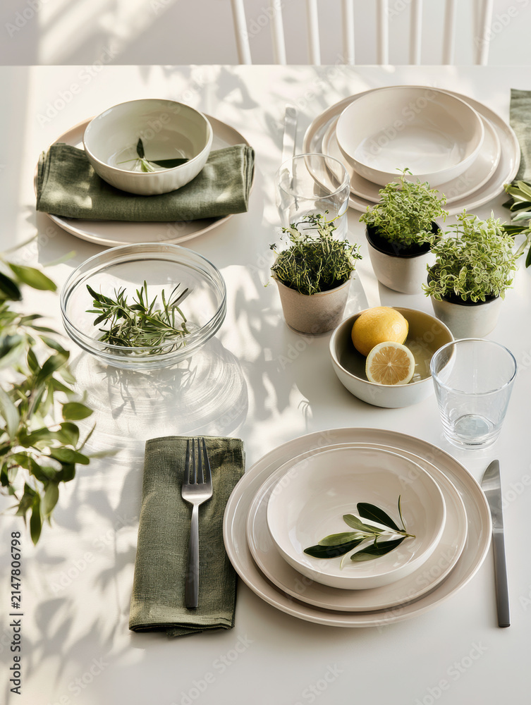 Obraz premium Fresh botanical kitchen table setting with ceramic plate, green napkin, herb plant, lemon, glassware, sunlight, and natural decor