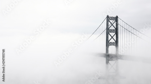 Suspension bridge tower emerging from thick fog in soft monochrome