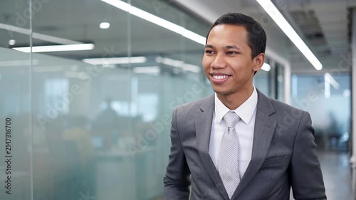 Indonesian business man investor, doubtful young male ceo executive wearing suit standing in office holding hand in chin looking away at work thinking on leadership question, feeling doubt.
