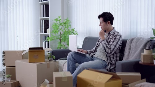 Young Asian man celebrating success while working on laptop surrounded by moving boxes in new apartment
