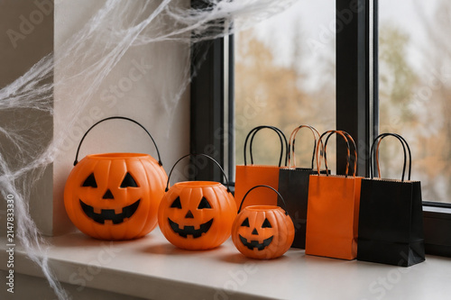 Pumpkin-shaped candy pails and orange gift bags with cobwebs on windowsill, Halloween retail display concept.