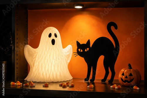 Paper ghost and black cat silhouette with candy corn and carved pumpkin, Halloween decor display concept.
