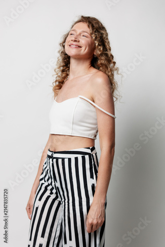 Quadro su tela A confident woman poses in a bright studio, wearing a white crop top and striped wide pants, smiling with relaxed charm