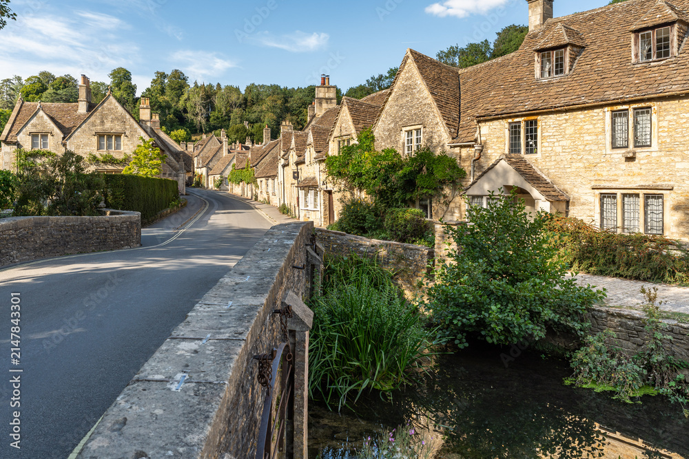 Fototapeta premium Scenic winding road through Castle Combe featuring iconic limestone houses and greenery, Cotswolds, England