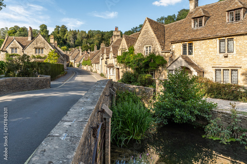 Scenic winding road through Castle Combe featuring iconic limestone houses and greenery, Cotswolds, England