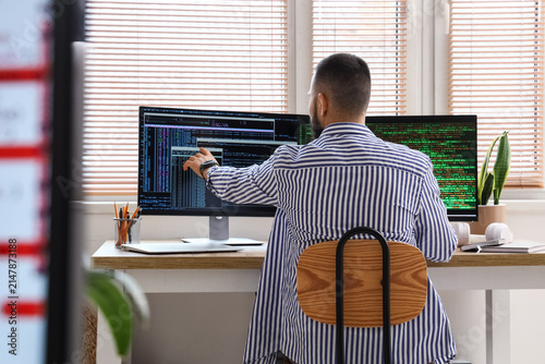Male programmer pointing at computer screen with code, software development a...