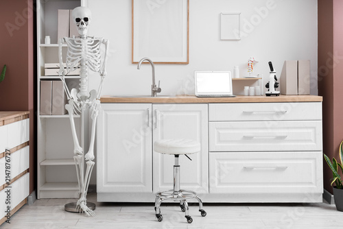 Interior of modern medical office with human skeleton model, shelf unit and w...