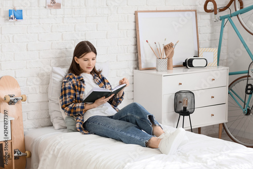 Beautiful young relaxed woman reading book and sitting on bed in bedroom