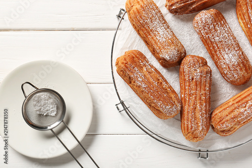 Foto Grid with tasty eclairs, sieve and sugar powder on white wooden background