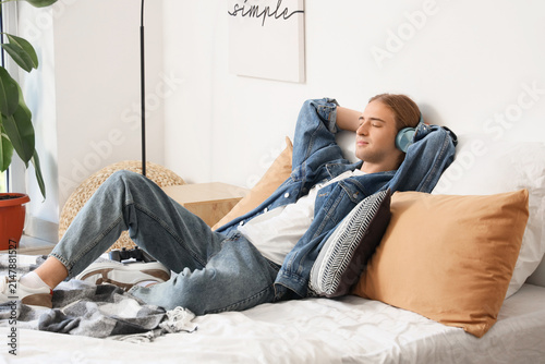 Young man with headphones listening to music in bedroom
