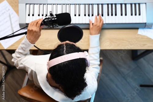 Fotografie Young woman with microphone playing synthesizer on table in recording studio, to