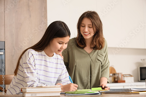 Teenage girl studying with tutor at table in kitchen