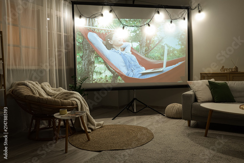 Interior of stylish living room with armchair, grey sofa and modern projector...