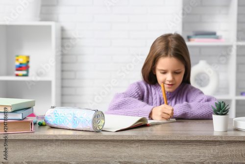 Cute little happy girl with pencil case, stationery and notebook doing homewo...