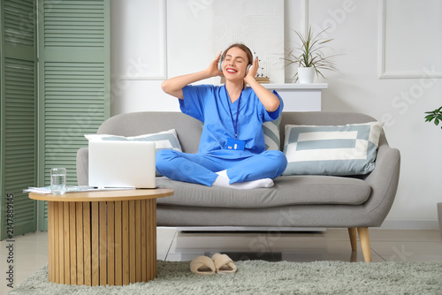 Young female medical student in headphones listening music near modern laptop...