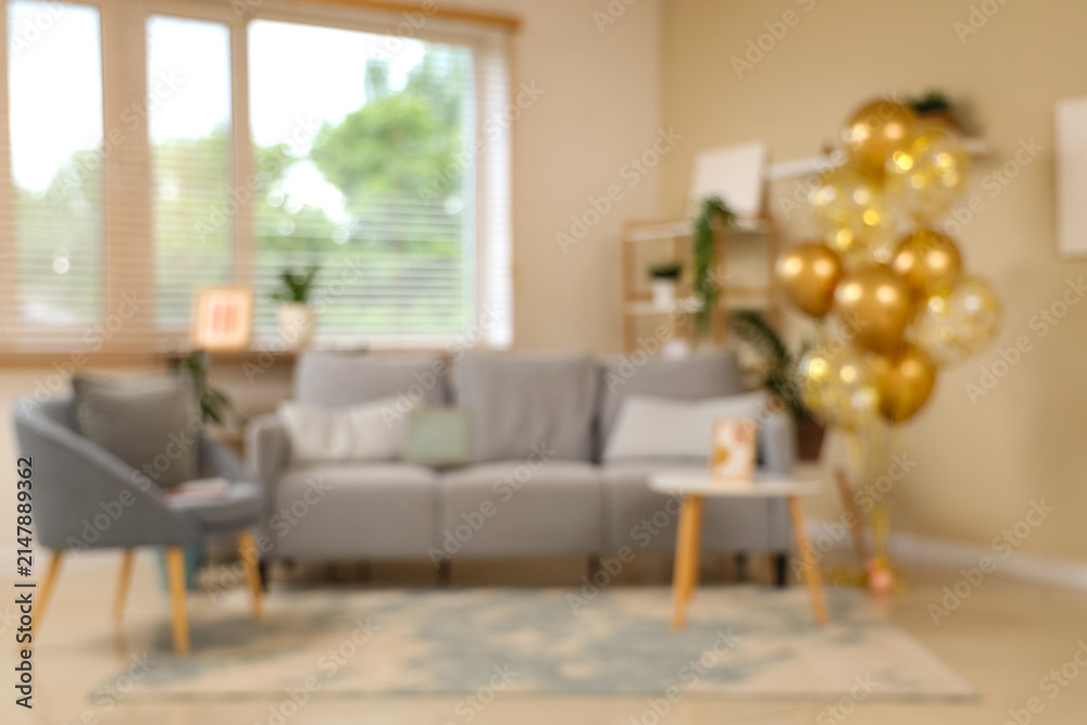 Obraz premium Beautiful golden air balloons with sofa and armchair near beige wall at home, blurred view